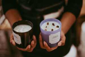 Person holding two custom candles with different containers, made at Cork and Candles.