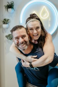 2 of the owners share a joyful moment at sēk Sauna Studio, with the man giving the man a piggyback ride.