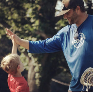 Coach gives a high-five to a young boy during a Scoops Lacrosse practice.