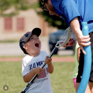 Boy laughs with coach during lacrosse practice.